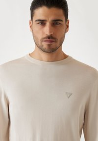 Maglione beige chiaro a maniche lunghe realizzato in un tessuto morbido. Presenta un collo rotondo e un piccolo logo triangolare sul petto.
