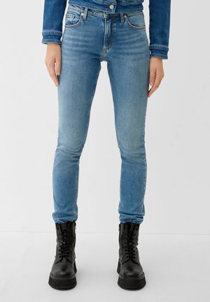 Woman wearing light blue skinny jeans, denim jacket, and black lace-up combat boots, standing against a plain background.