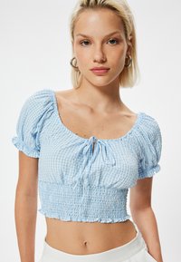 Blaues karierter Crop-Top mit Puffärmeln, gerafftem Oberteil und Bindedetail am Ausschnitt. Verfügt über einen Rüschensaum und weichen Baumwollstoff.