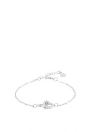 Silverfärgad armband med en delikat kedja, med ett hjärtformat länknäste i mitten. Slät yta och justerbart lås med en liten berlock.