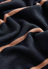 Tă fabricată din tricot cu o bază de culoare bleumarin închis și dungi orizontale de piersică deschisă. Textură moale cu detalii de cusătură vizibile și cădere ușoară.