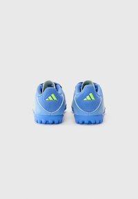 Zapatillas deportivas azules con material texturizado, acentos verdes y suela de goma con pequeñas protuberancias; la vista trasera presenta el logo de tres rayas.