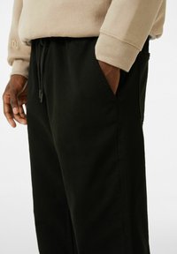 Joggers en tissu noir à coupe décontractée, dotés de poches latérales et d'une taille élastique avec cordon de serrage. Accompagnés d'un sweat-shirt beige au-dessus.