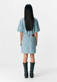 Vestido de mezclilla en azul claro con estampado floral; mangas cortas, cintura ceñida y corte recto. Botas negras hasta la rodilla completan el look.