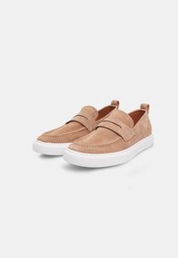 Suede slip-on skor i ljus beige med en vit gummisul. Har stickade detaljer och dubbla sidoflikar för enkel påtagning.