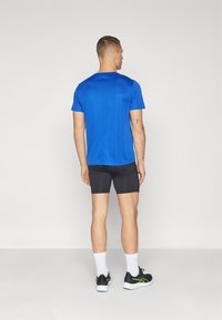 Blå kortärmad idrottströja med rund hals, matchad med svarta shorts. Modellen står med ryggen mot kameran och visar en jämn textur.
