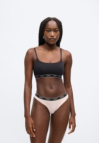 Zwarte bralette met dunne bandjes en een logoband, gecombineerd met een lichtroze string met een zwarte logoband. Glad stof, nauwsluitend ontwerp.