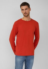 Rotes Langarm-T-Shirt aus leichtem Baumwollmaterial. Mit Rundhalsausschnitt und lässiger Passform, kombiniert mit blauen Jeans. Sanfte Textur.