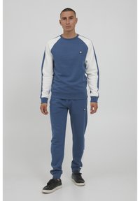 Blå sweatshirt med hvite raglanermer, ribbede mansjetter og rund hals. Matchende blå joggebukser med elastisk liv og logo på begge plagg.