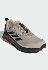 Jasnobeżowe buty sportowe z czarnymi akcentami, z siateczkową cholewką i gumową podeszwą. Posiada uchwyt na pięcie i geometryczny wzór z boku.