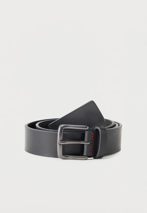 Črni usnjeni pas, zvit, z kovinsko pravokotno zaponko in majhnim rdečim šivom na zanki, na belem ozadju.