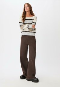 Pleta sweater s krem, sivim i smešnim prugama; široke smeđe pantalone; masivne crne platforme; teksturirana tkanina i opušten kroj.