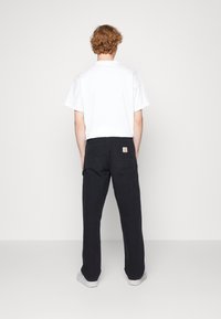 Černé cargo kalhoty s několika kapsami, se štítkem s logem na zadní straně. Kombinovány s jednoduchým bílým tričkem s krátkým rukávem.