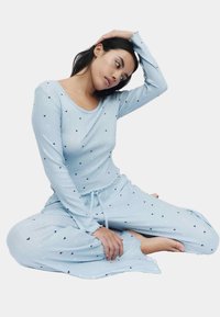 Lichtblauw loungewear set gemaakt van zachte stof, met lange mouwen en lange broek. Voorzien van kleine zwarte hartjespatronen en een taille met trekkoord.