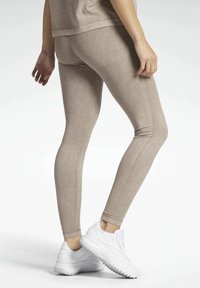 Beżowe legginsy o gładkiej fakturze, dopasowanym kroju i subtelnym połysku. Połączone z białymi trampkami z masywną podeszwą.