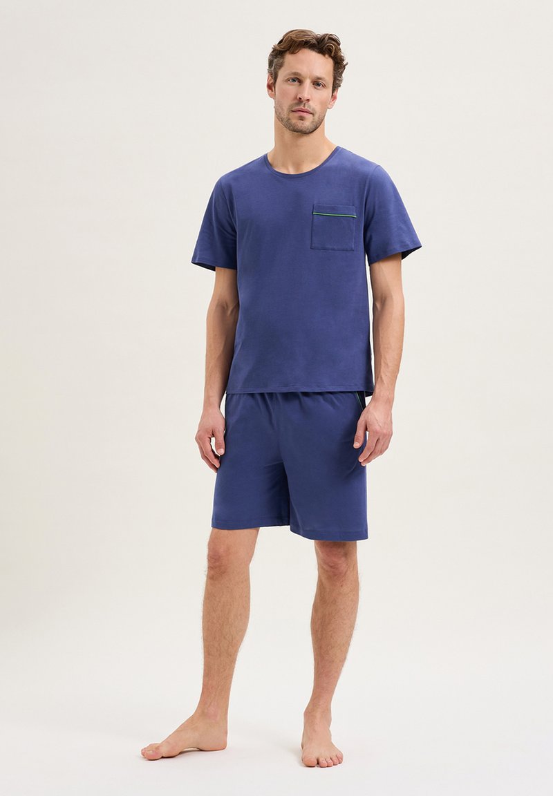 Ensemble de vêtements de loisirs en coton marine comprenant un T-shirt à manches courtes avec une poche sur la poitrine et un passepoil vert contrastant, assorti de shorts.