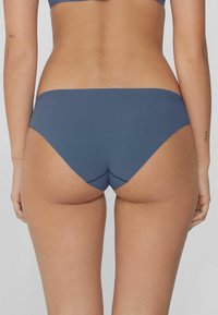 Šedé bikini kalhotky s hladkým povrchem, nízkým střihem a kontrastním šitím. Mají V-říznutí na zadní části a minimalistický design.