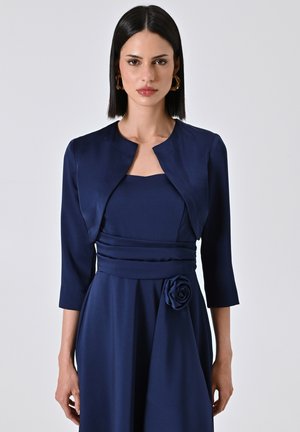 Navy blue dress with a fitted bodice and a rose detail at the waist, paired with a structured cropped jacket in the same fabric.