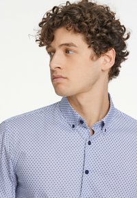 Camicia pattern blu chiaro con colletto button-down. Presenta un design geometrico, bottoni blu e una texture di tessuto liscia.