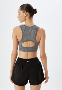 Grå sport crop top med rygåbning, parret med sorte løstsiddende shorts udstyret med elastisk talje og logo-detalje.