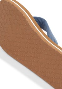 Blå canvas flip-flop med en texturerad brun gummisole, med en vit rand nära kanten och en rektangulär design för grepp.