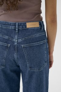 Džínové kalhoty v tmavě modré barvě s volným střihem. Mají koženou etiketu s nápisem "InWear", zadní kapsy a viditelné švy.