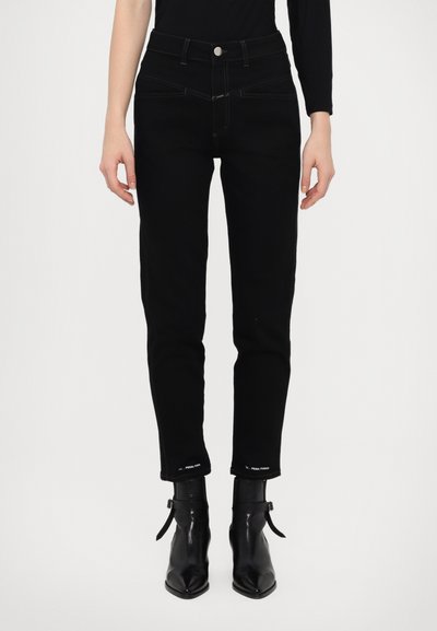Fekete farmernadrág magas derékkal, slim fit szabással, kontrasztos varrással és logo részletekkel a szárak végén. Fekete bokacsizmával viselve.