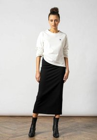 Hvid langærmet skjorte med et lille logo, parret med en tætsiddende sort midi-nederdel og sorte ankelstøvler; glatte teksturer, enkel design.