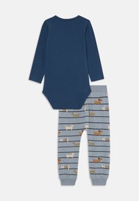 Bodysuit pour bébé à manches longues bleu marine associé à un pantalon bleu clair avec des motifs de chiens teckels et le texte "Woof".