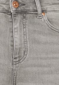 Tela de mezclilla gris con una textura sutil, que presenta un botón de cobre y detalles de costura, y un contorno de bolsillo delantero.