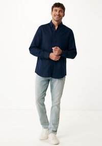 Marineblauwe langärmige blouse met knoopkraag, gecombineerd met lichtblauwe jeans en witte sneakers. Glad materiaal, normale pasvorm.