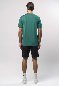 Groen atletisch shirt met korte mouwen gecombineerd met zwarte shorts. Het shirt heeft een gladde textuur en een losse pasvorm, geschikt voor sportieve activiteiten.