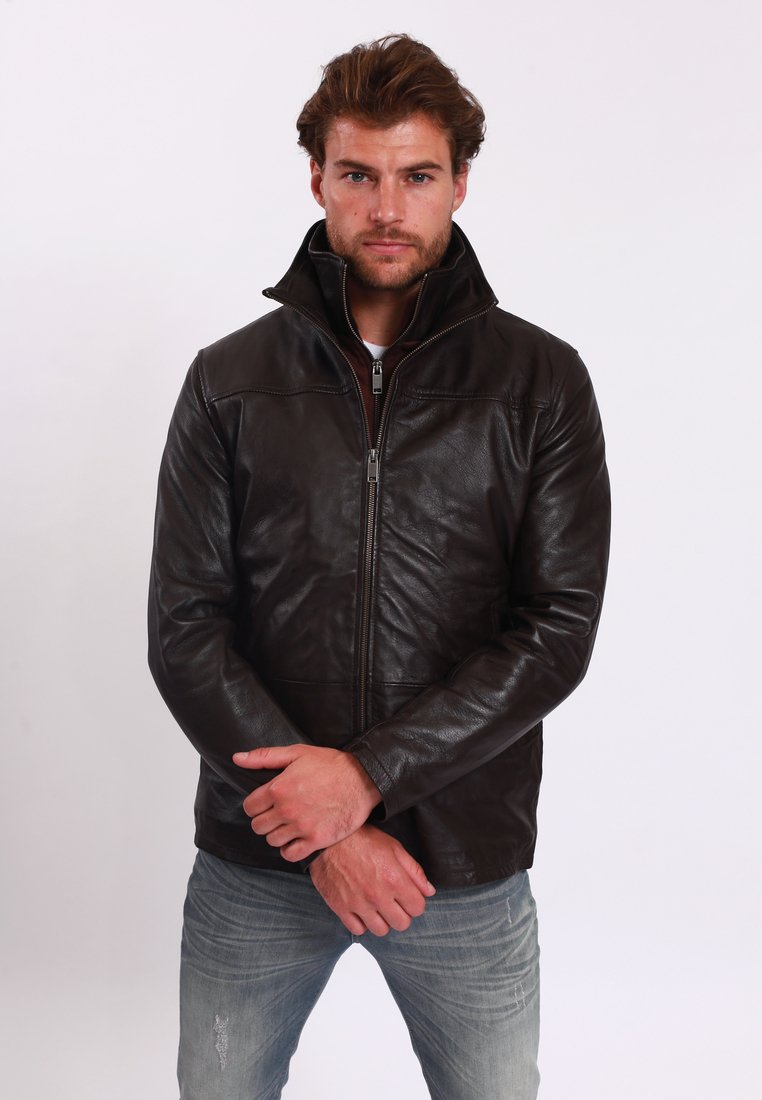 Brun läderjacka med hög krage, framdragkedja och subtila sömdetaljer. Bärs med ljusblå jeans. Slät textur.