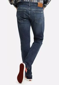 Ciemnoniebieskie dżinsy o slim fit, z tylnymi kieszeniami i skórzaną metką na pasku. Noszone z ciemnymi sneakersami.