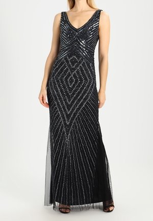 Slim black evening gown with silver sequin geometric patterns, sleeveless V-neck, and floor-length sheer overlay, worn with black open-toe heels.