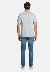 Camiseta de manga corta azul claro con cuello redondo, combinada con jeans azules ajustados y zapatillas blancas, vista desde atrás.