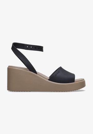 Sandales compensées noires avec une large bande avant, une sangle arrière à la cheville avec boucle réglable et une semelle plate beige. Fabriquées en matériau léger.