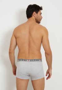 Gray cotton boxer briefs with a navy waistband featuring the "GUESS" logo in red. Smooth texture, fitted design, and mid-rise cut.