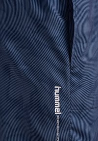 Marinblå idrottsshorts med vertikala ränder, med en vit "hummel"-logotyp. Tillverkade av lätt, slätt tyg med en funktionell design.