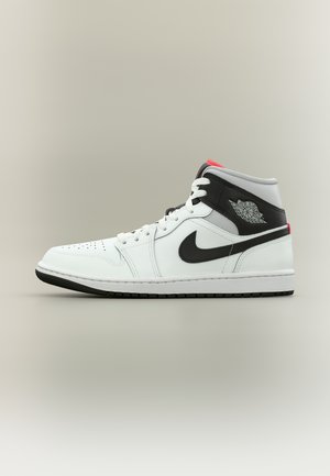 Scarpa da ginnastica alta bianca e nera con logo Air Jordan, swoosh Nike nero, lacci bianchi e accenti rossi sulla linguetta e sul tallone.