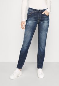 Blå denimjeans med slim fit, som har knap- og lynlåsstängning, fem fickor och subtila slitna detaljer, ihop med vita sneakers.