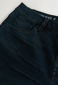 Tumesinised teksapüksid, millel on sile tekstuur, esitasku, nööpidega kinnis ja õmbluste ääres peened õmblused.