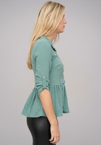 Camicia button-up turchese con orlo pieghettato, maniche a tre quarti e dettaglio con risvolto, abbinata a leggings neri.