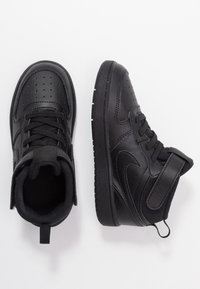 Tênis de couro preto de cano médio com detalhes perfurados, atacadores planos, uma tiras com velcro e solas de borracha texturizada.
