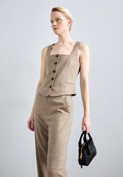 Chaleco de tela texturizada beige con escote cuadrado y botones negros; combinado con pantalones de talle alto a juego y un pequeño bolso negro.