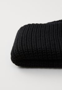 Texturiertes schwarzes Strickgewebe mit einem gerippten Design, das ein dickes, gemütliches Aussehen und eine glatte Verarbeitung an den Kanten zeigt.
