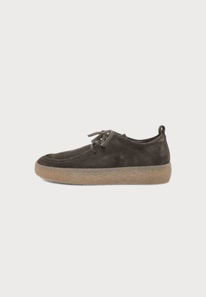 Chaussure en daim marron foncé à lacets avec semelle en caoutchouc beige épaisse et texturée et languette au talon, vue de profil sur fond blanc.