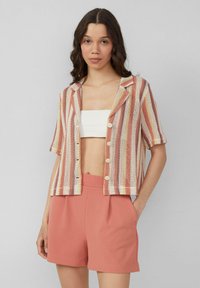 Gestreept overhemd met korte mouwen in koraal, crème en gele geweven stof, voorzien van een kraag en knoopsluiting aan de voorkant, gedragen met koraalkleurige shorts.