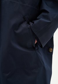 Mornarsko modra vodoodporna jakna z gumbom, stranskimi žepi in strukturirano tkanino, ki prikazuje eleganten, poenostavljen dizajn.