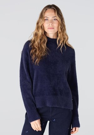 Marineblauwe, donzige trui met een hoge hals, lange mouwen en een relaxte pasvorm. Heeft een geribde zoom en boorden voor extra textuur.